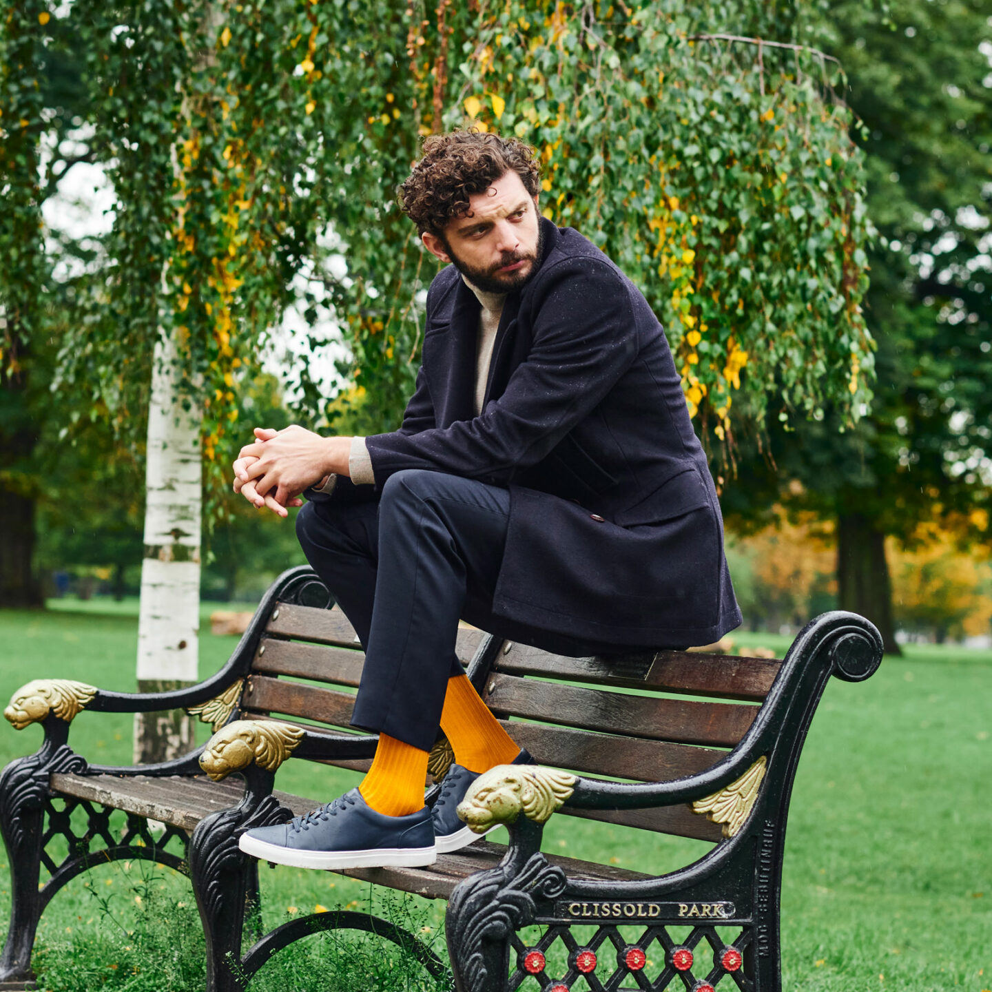 Michael C Fox on a park bench wearing yellow socks