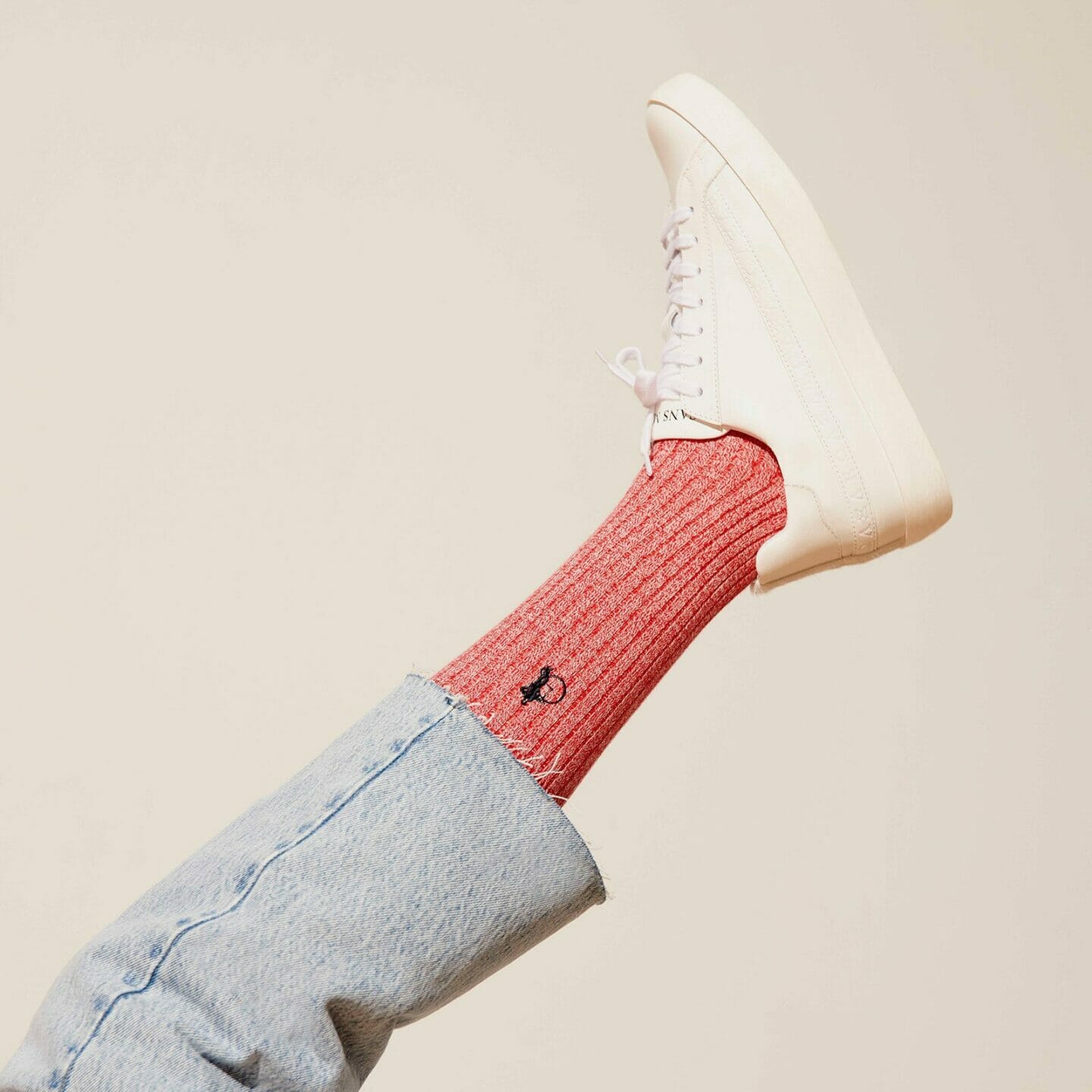 A leg extended into the air, with a Marl Red sock, white trainer and light blue