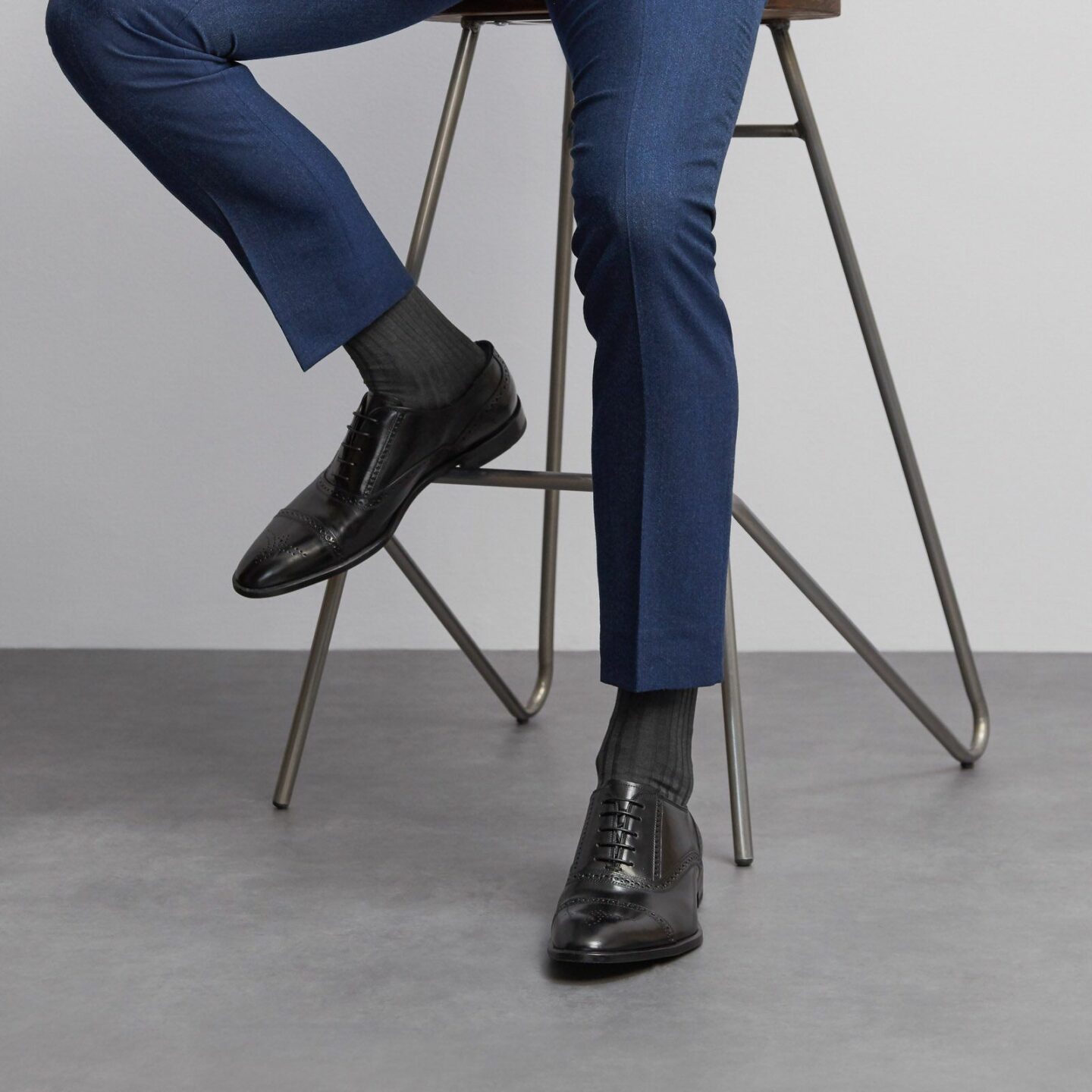 Man in a navy suit sitting on a stool wearing canon ball black socks