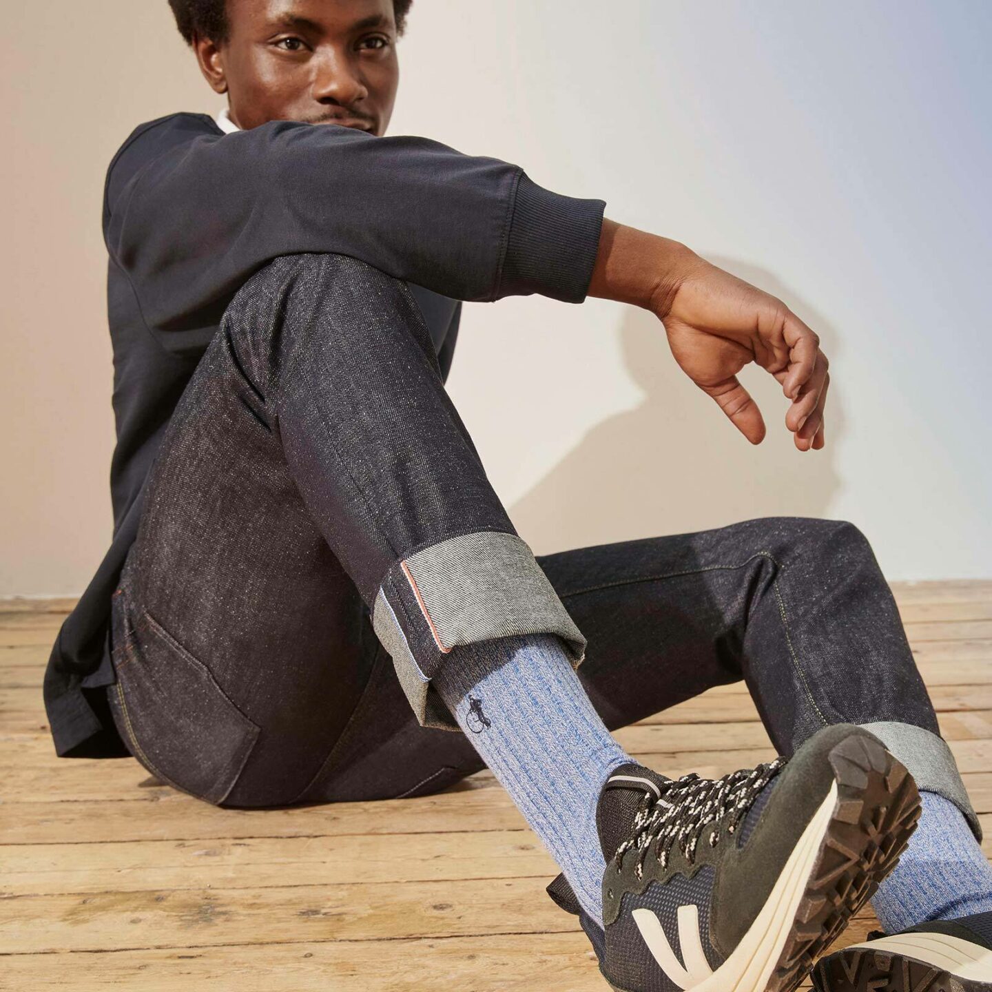 Man sitting on a wooden floor, resting his arm on his knee wearing marl denim blue socks