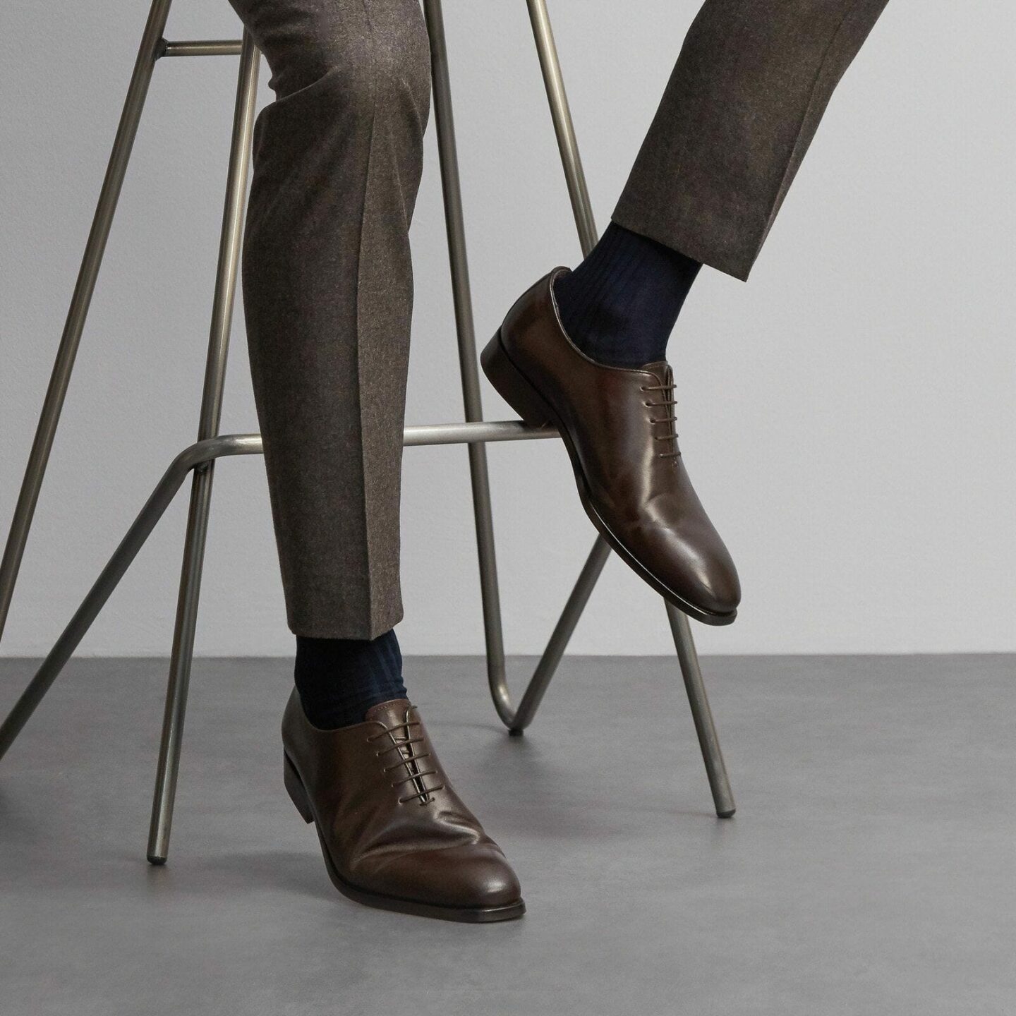 Close up of a man sitting on a stool wearing a dark grey suit and navy cotton socks