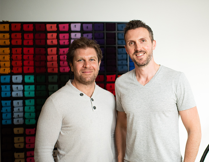 Founders of London Sock Company, Ryan Palmer and Dave Pickard standing in front of a wall of colourful socks.