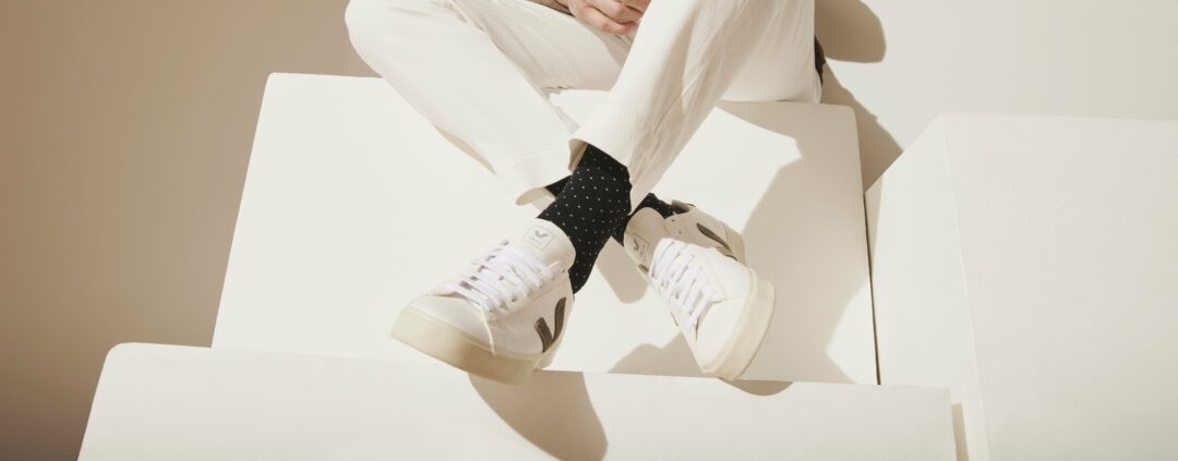 A man in a suit sitting on white boxes wearing spotted long black socks and white trainers.